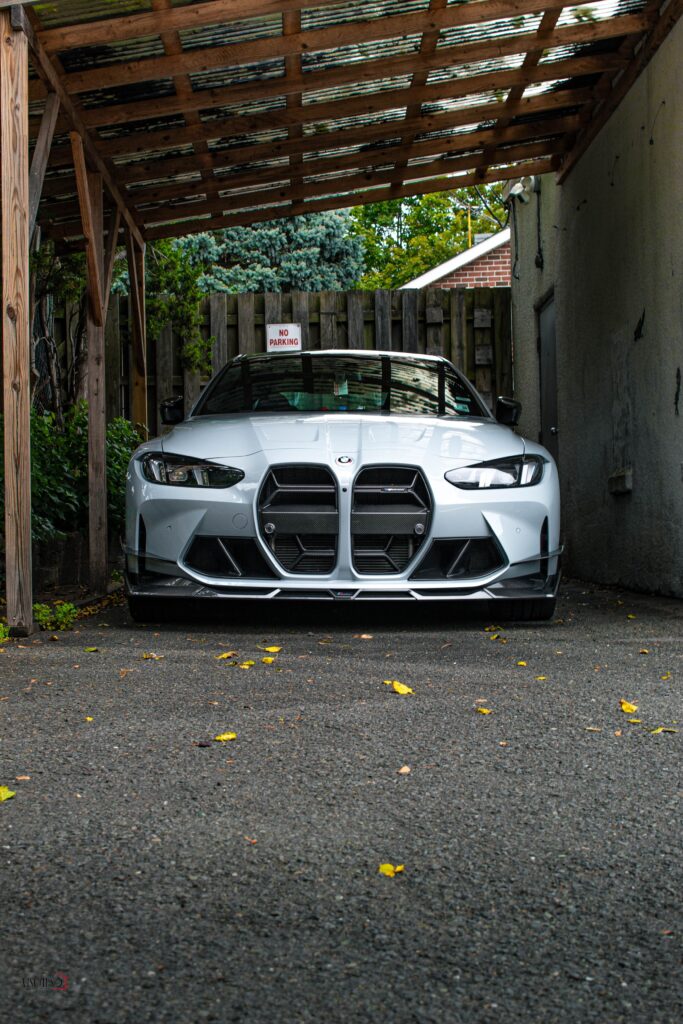 Front view of a sleek silver car parked under a wooden carport in an outdoor setting.