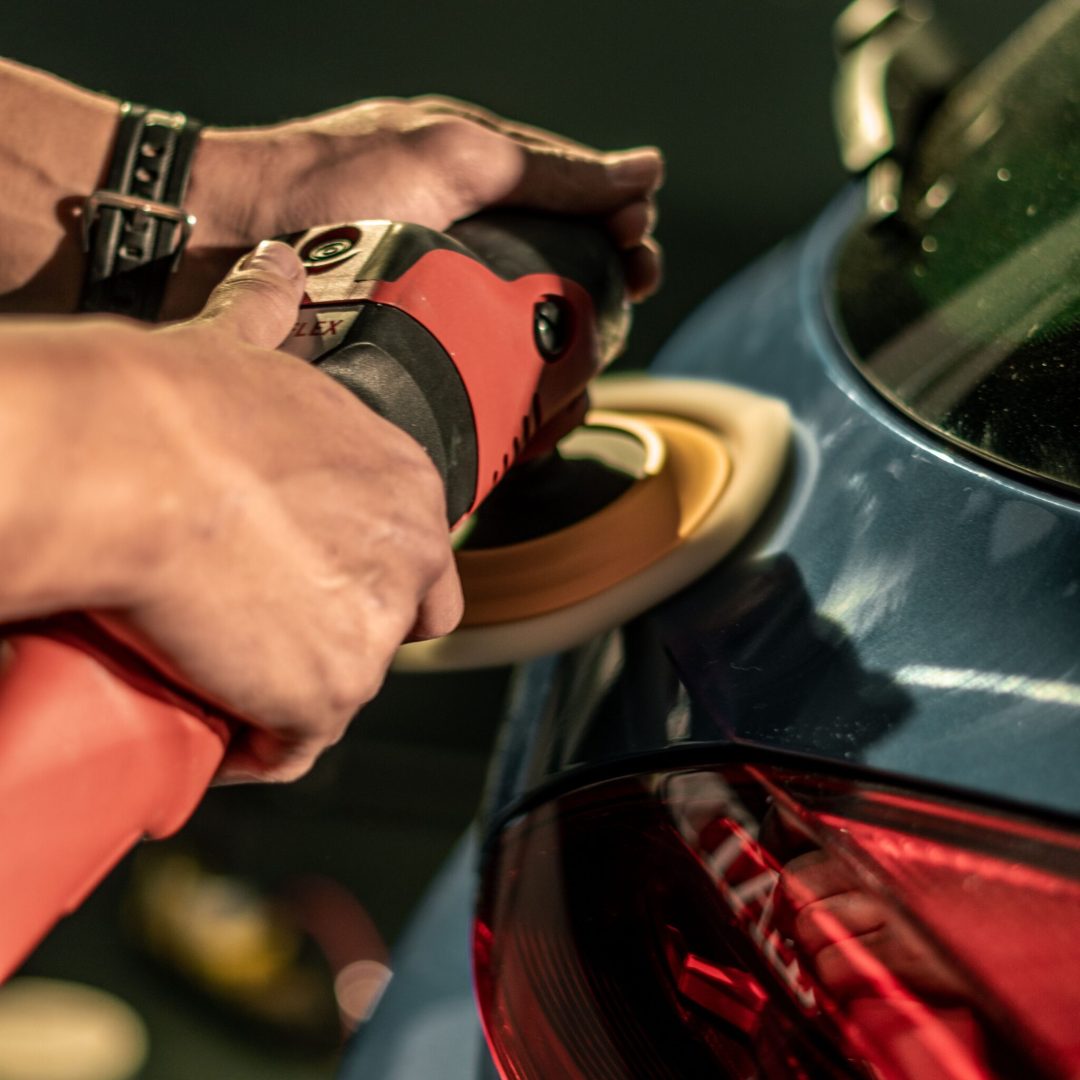 Hands using a buffing machine to polish a car for a glossy finish, highlighting car detailing process.
