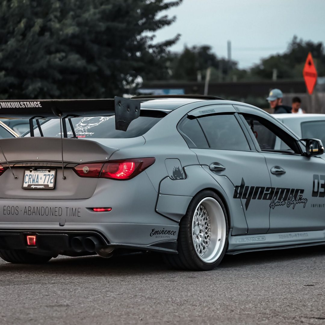 A modified sports car with custom wrap and spoiler parked on asphalt, perfect for automotive enthusiasts.