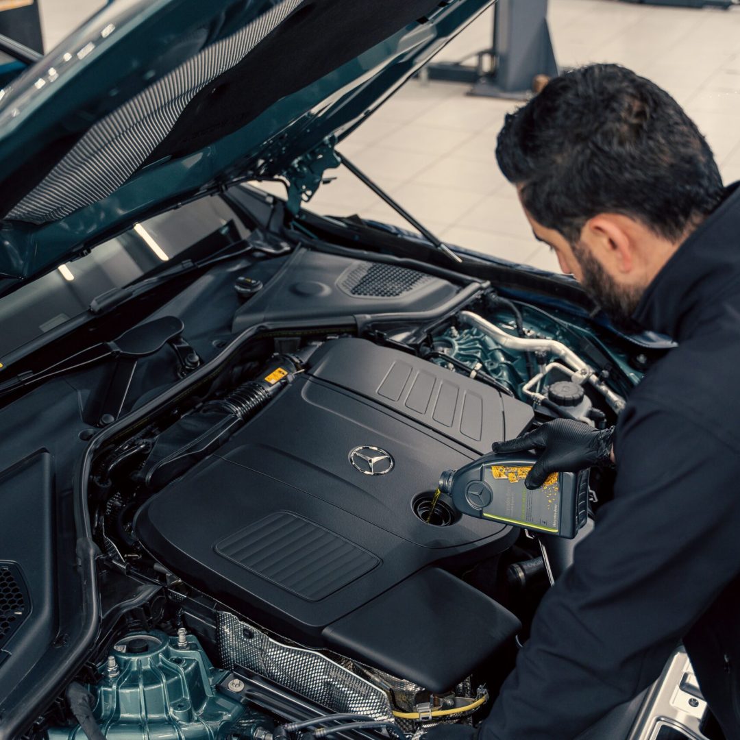 Mechanic inspecting and filling engine oil in a car at an indoor service center.