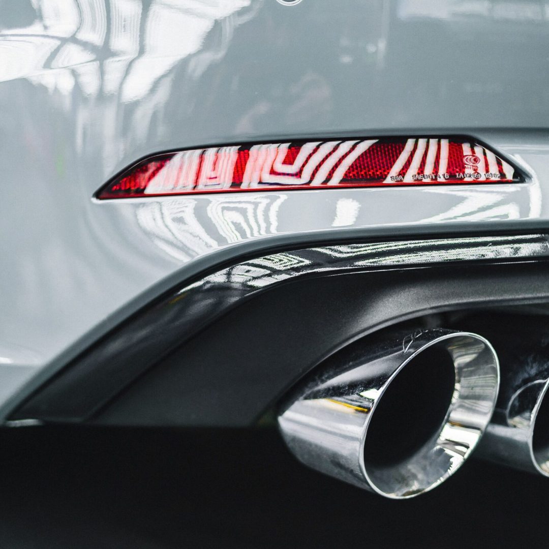Detailed view of a car's exhaust pipes and rear taillight with reflections.