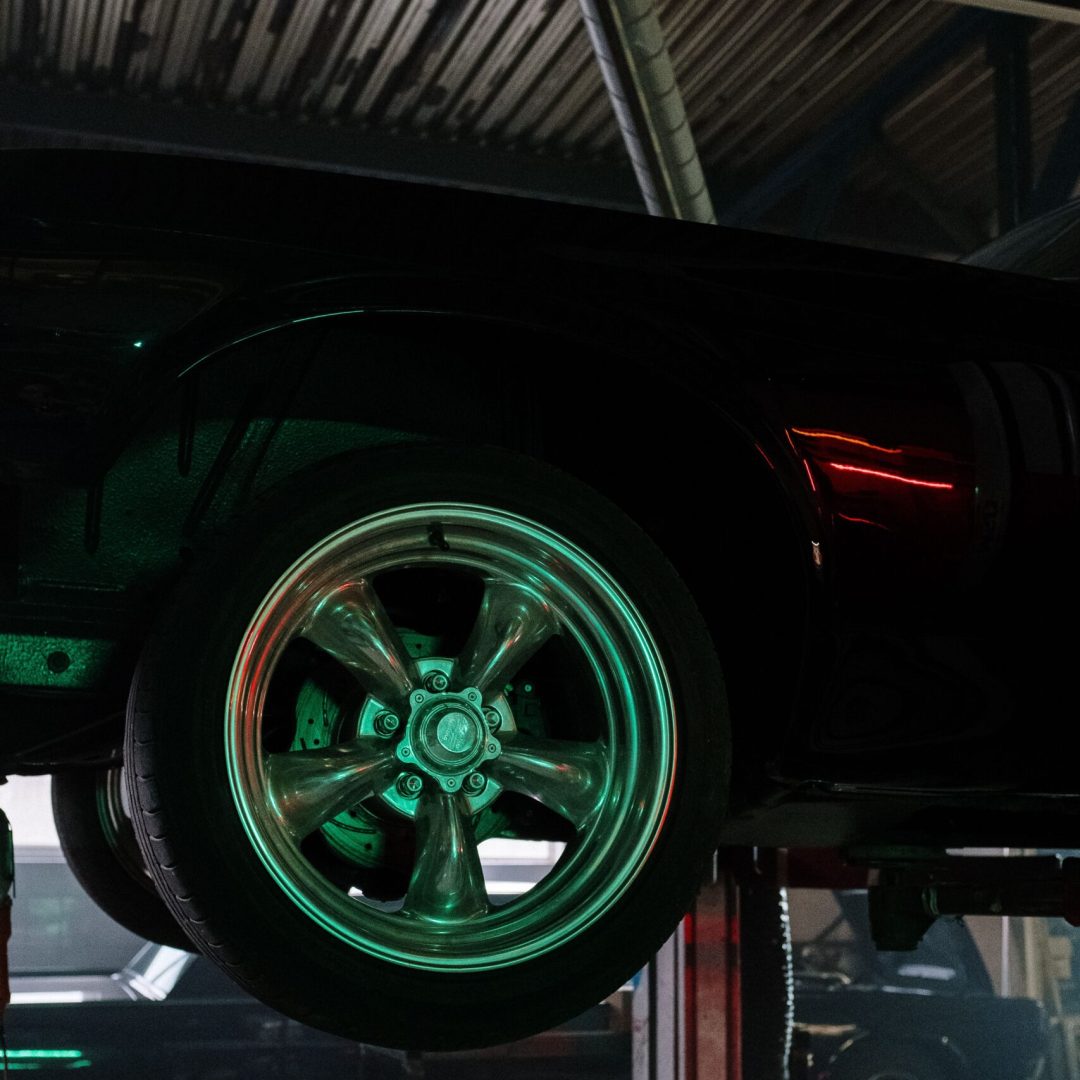 Close-up of a car wheel illuminated by neon lights in a garage.