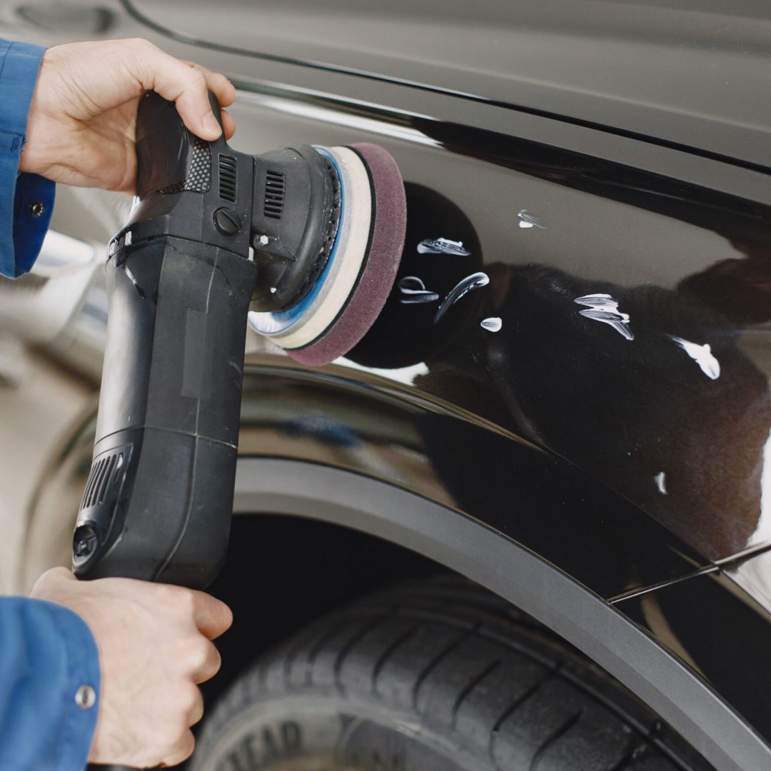 Hands using a polishing machine on a car's surface in a garage setting.